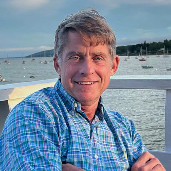 Headshot of Sean Fawcett, Yacht Consultant based in Manchester, MA, with a harbor full of boats in the background.
