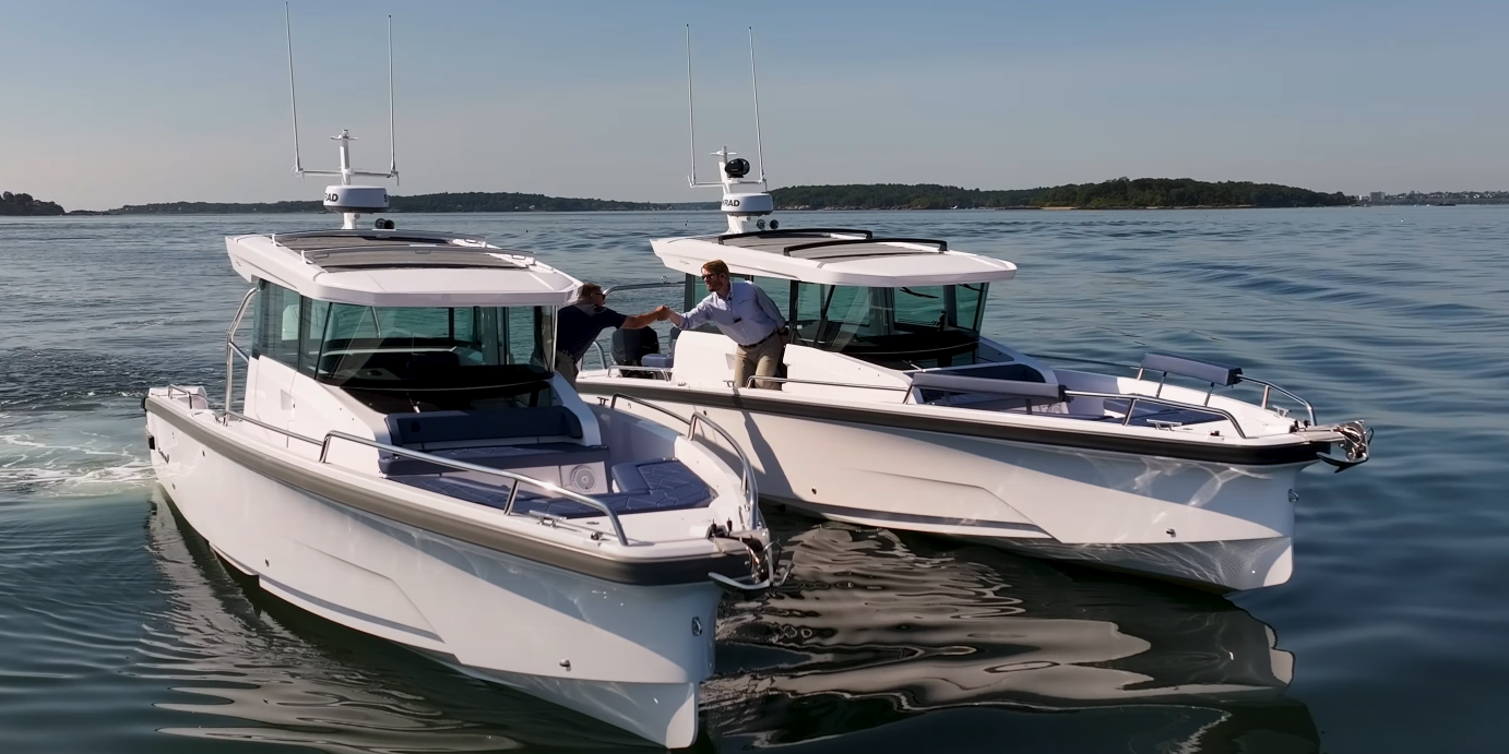 Two Axopar 29s abreast in the water with Yacht Consultants Mike Porter (Portsmouth, RI) and Ben Scheffer (Camden, ME) shaking hands over the water between the boats, filmed from in front during a twin-engine vs single-engine race.