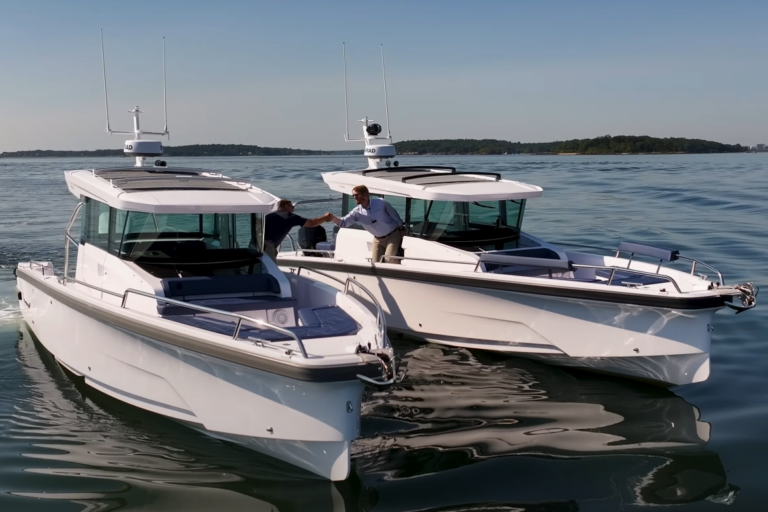Axopar 29 Twin vs Single Engine Race – Handshake Moment Two Axopar 29s abreast in the water with Yacht Consultants Mike Porter (Portsmouth, RI) and Ben Scheffer (Camden, ME) shaking hands over the water between the boats, filmed from in front during a twin-engine vs single-engine race.