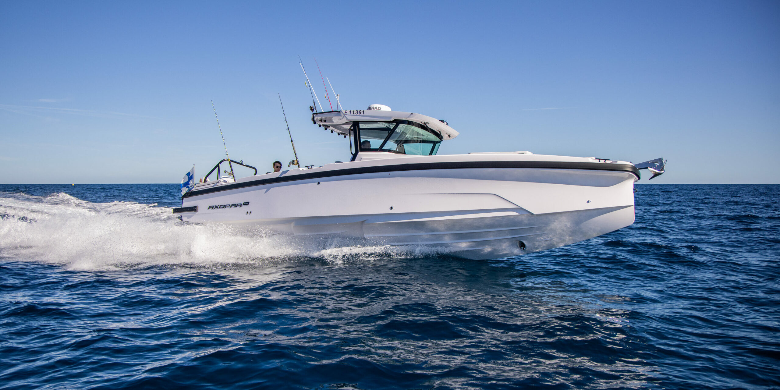 Axopar 29 CCX (Center Console) running through deep blue ocean on starboard side with Finnish flag visible on the stern, under a clear blue sky.