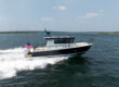 Side view of a Targa 32 Outboard cruising in Casco Bay, Maine, showing the full boat, twin Mercury 350 outboards, and an American flag flying from the stern.